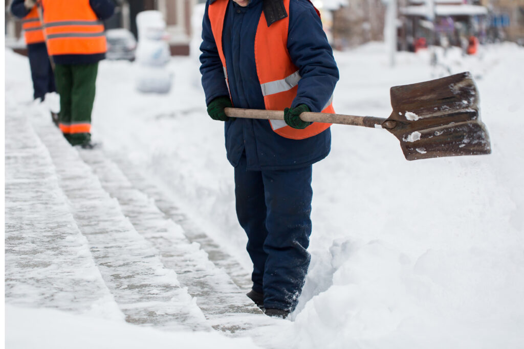 Employees of municipal services in a special form are clearing snow from the sidewalk with a shovel